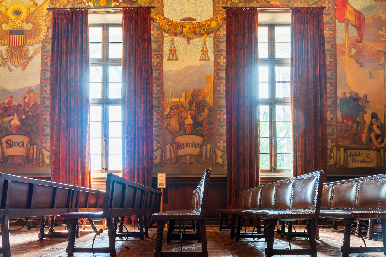 The windows of the mural room look on to the benches of the room. 100 year old curtains line the windows and the walls are covered in murals.
