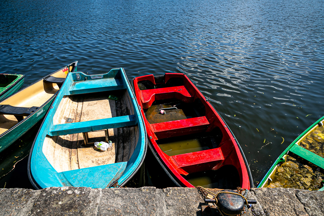 Boats of different colours tied up next to the banks of a river.