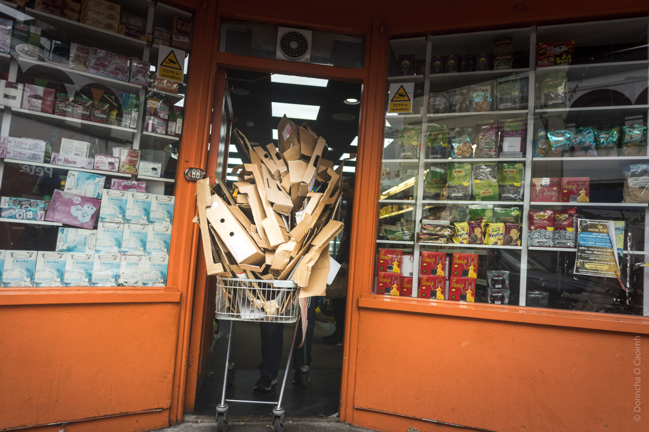 A shoppy trolley is pushed out the door of a shop with a large pile of cardboard 