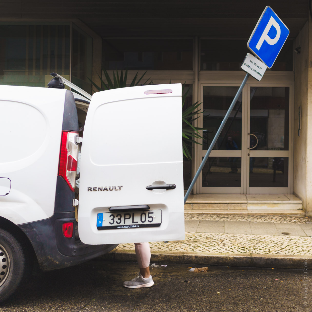 Humorous street photo: Person's legs visible behind an open white Renault van door with Portuguese licence plate, next to a parking sign in Lisbon.