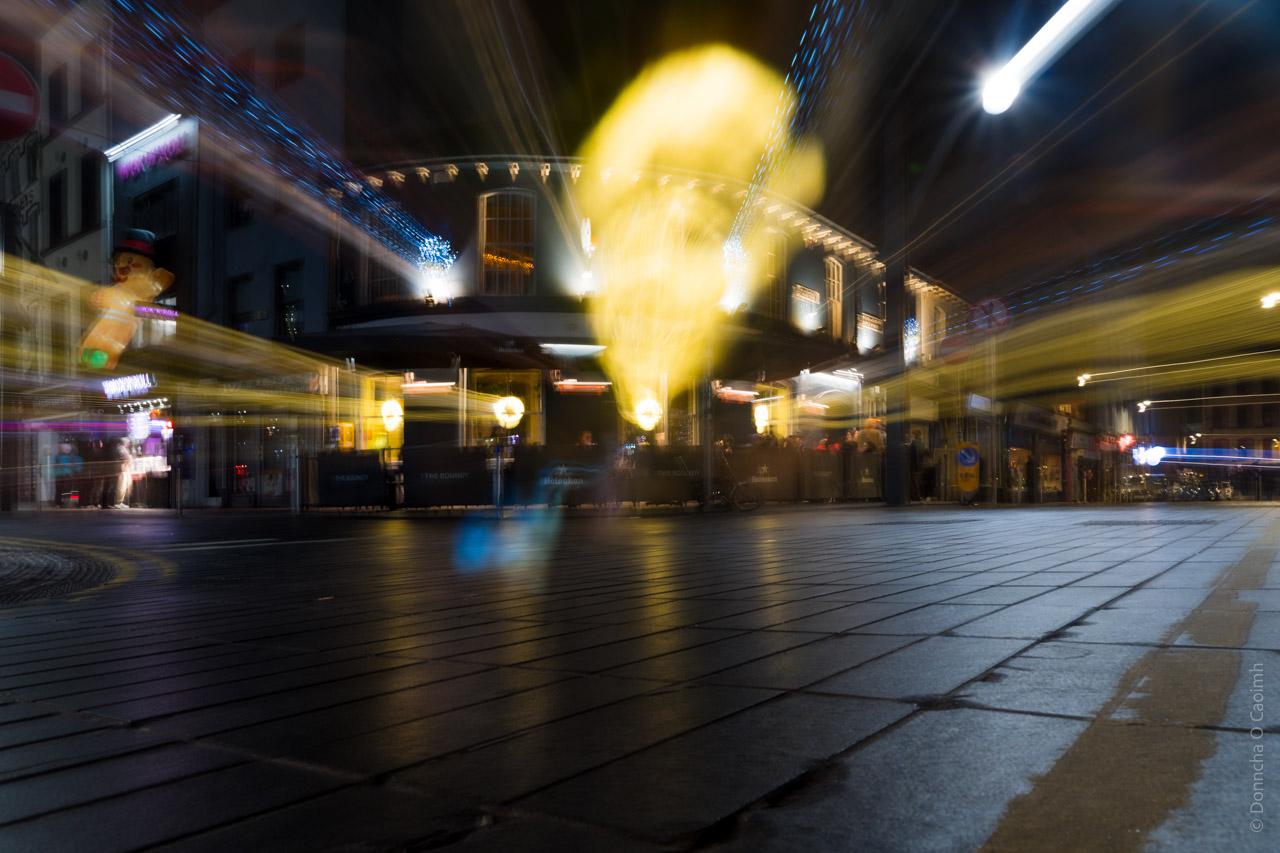 An impressionistic long exposure shot of a Cork city centre street at night, featuring blurred lights and the pub "The Roundy".