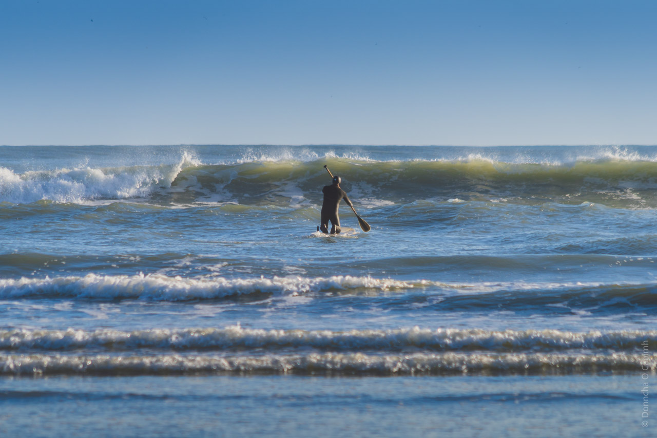 A person paddleboarding in the ocean, with waves breaking in the background