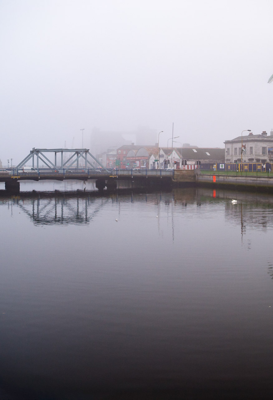 2005 photograph of Cork City Hall with its distinctive green dome reflected in the River Lee, showing construction cranes and the area before The Elysian development and modernisation, with swans visible on the calm water (1/3)