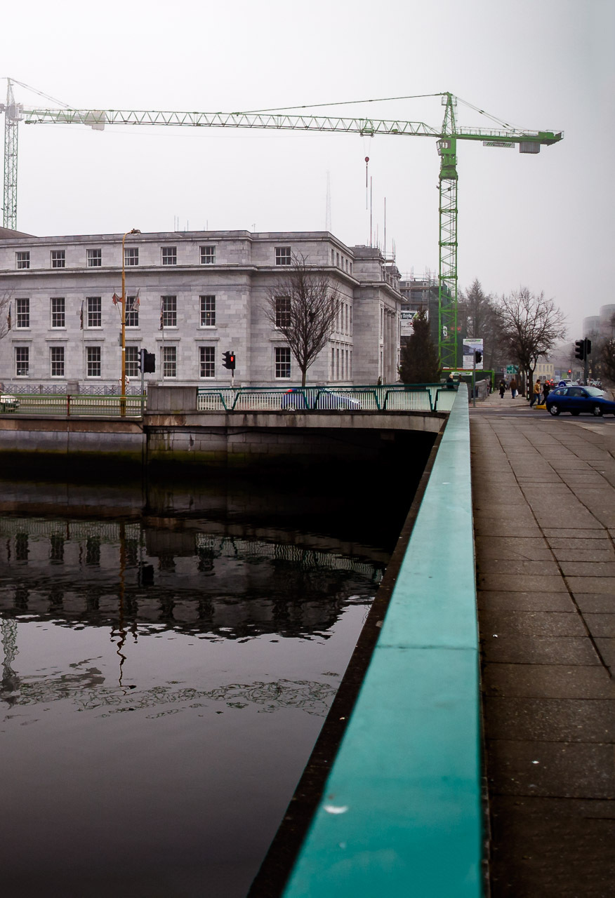 2005 photograph of Cork City Hall with its distinctive green dome reflected in the River Lee, showing construction cranes and the area before The Elysian development and modernisation, with swans visible on the calm water (3/3)