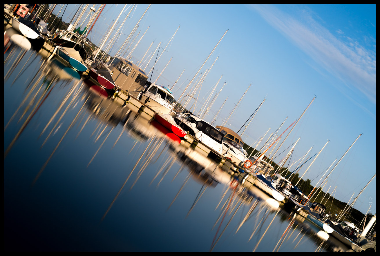 Marina scene in Kinsale showing sailing boats and yachts with tall masts reflected in calm water under a blue sky with wispy clouds in County Cork.