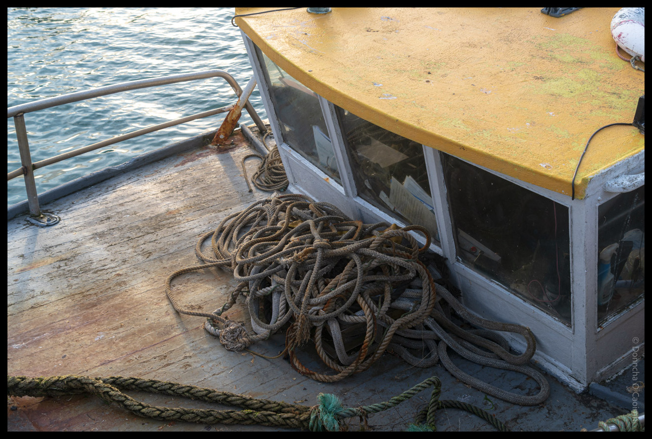 Coiled ropes and fishing equipment on the deck of a working boat with yellow wheelhouse structure in Ballycotton harbour, County Cork
