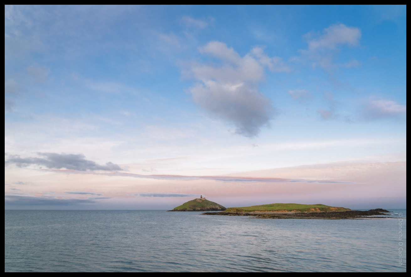 Ballycotton Lighthouse standing on a small green island surrounded by calm waters under a pastel evening sky with soft clouds after sunset, County Cork.