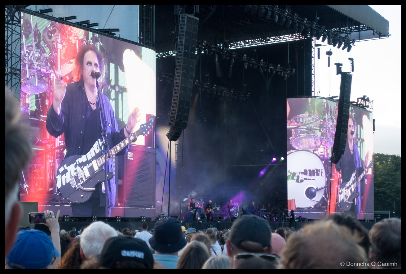 Looking that stage where tiny figures perform but Robert Smith is pictured on the large screens to either side of the stage.