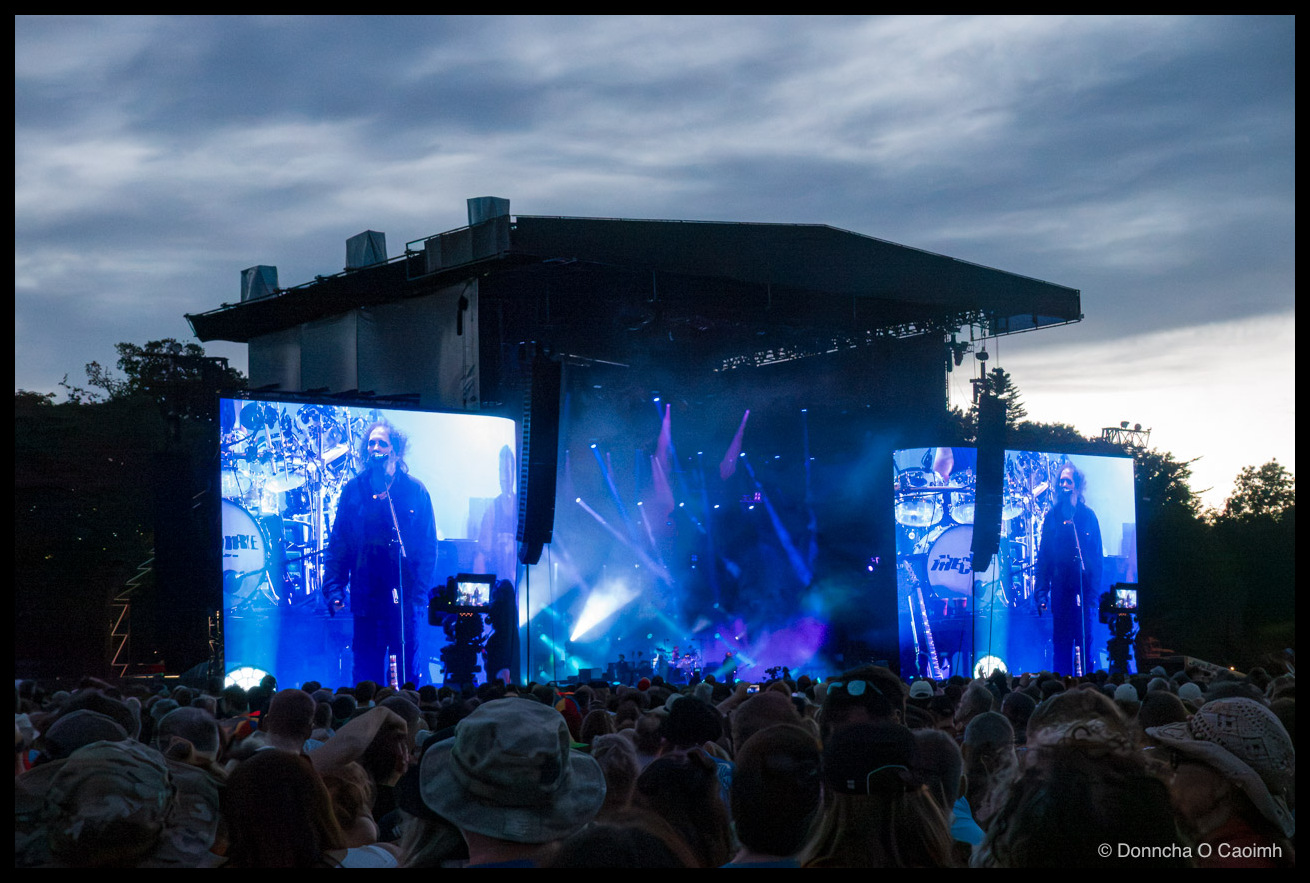 The stage, big screens. Robert Smith on the screens. Crowd in front.