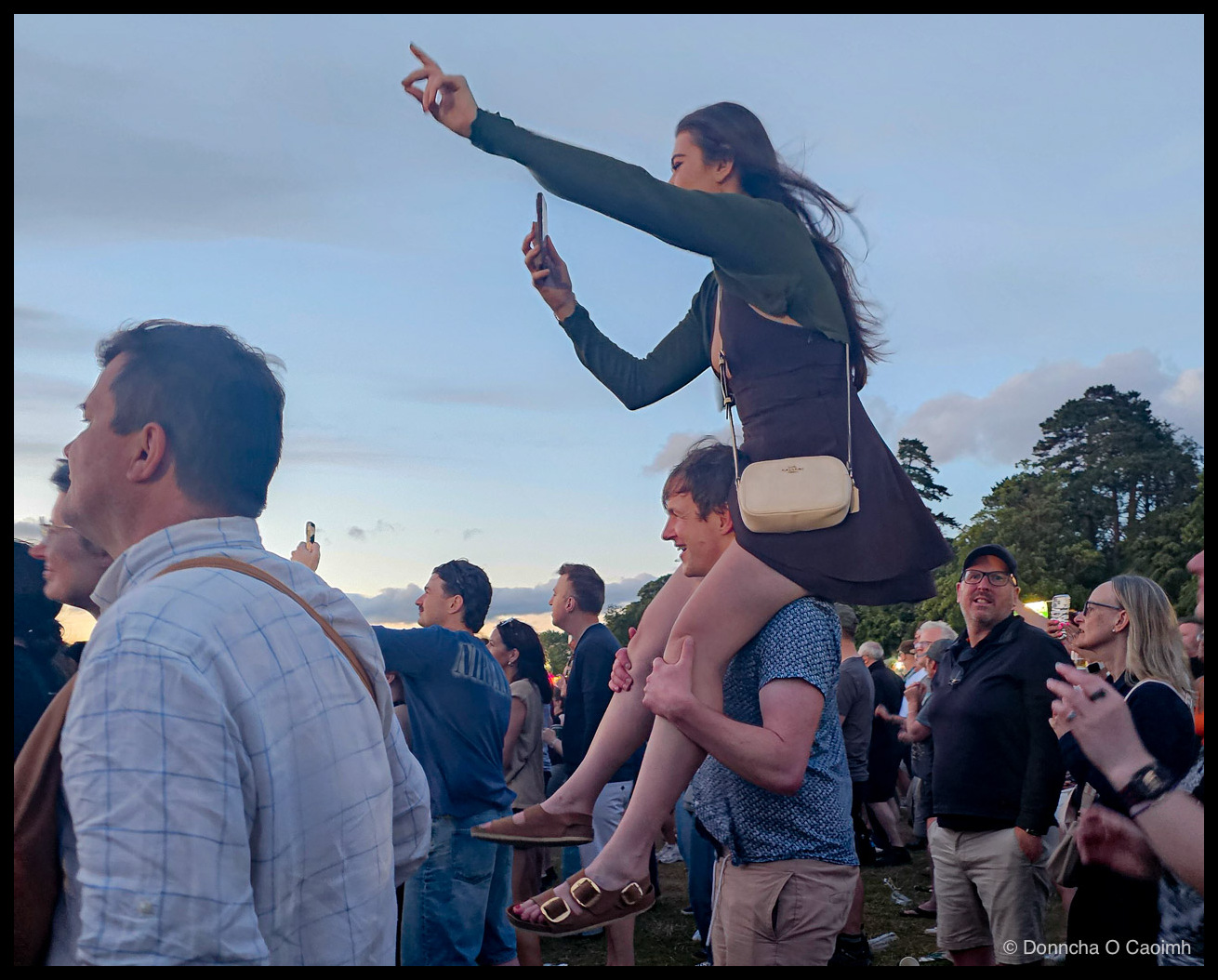 A woman sitting on a man's shoulders to get a better view.